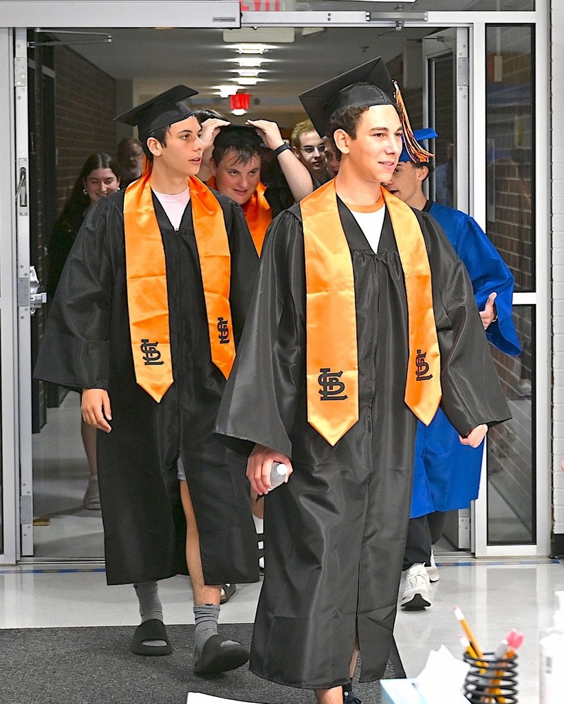 seniors in graduation robes walk through school doors