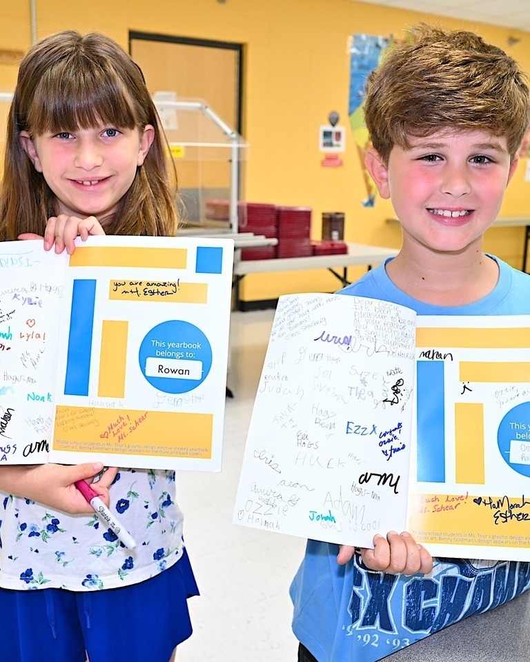 students hold up their signature-covered yearbooks