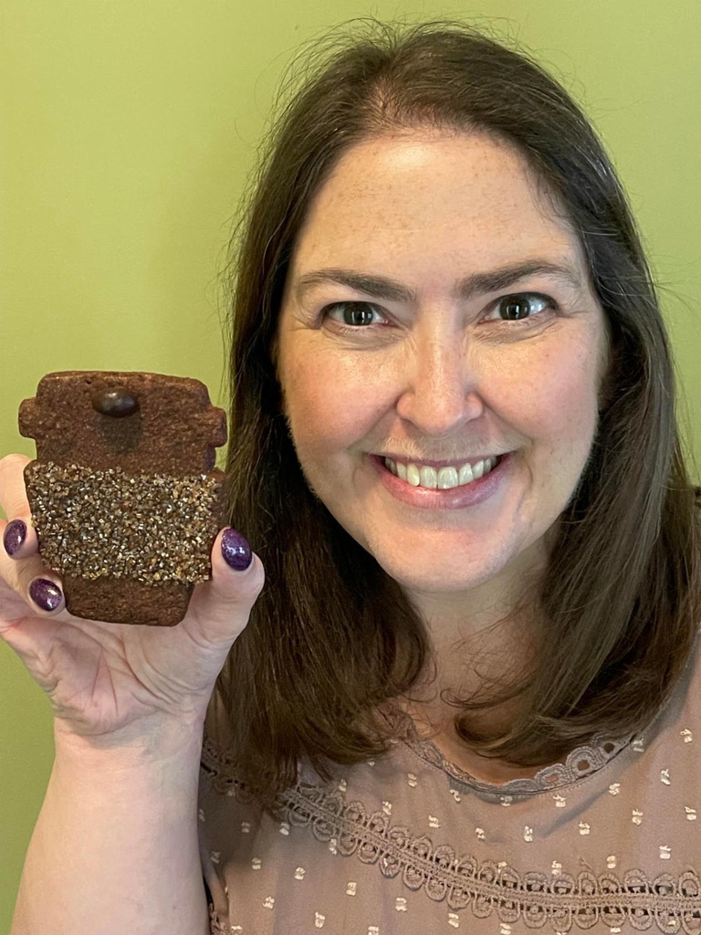 Teacher Jenny Palmer holds brown coffee cup shaped cookie