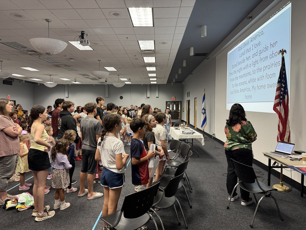 students and teachers stand and sign God Bless America