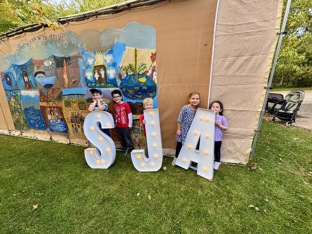 students outside of sukkah pose with S J A marquee lettters