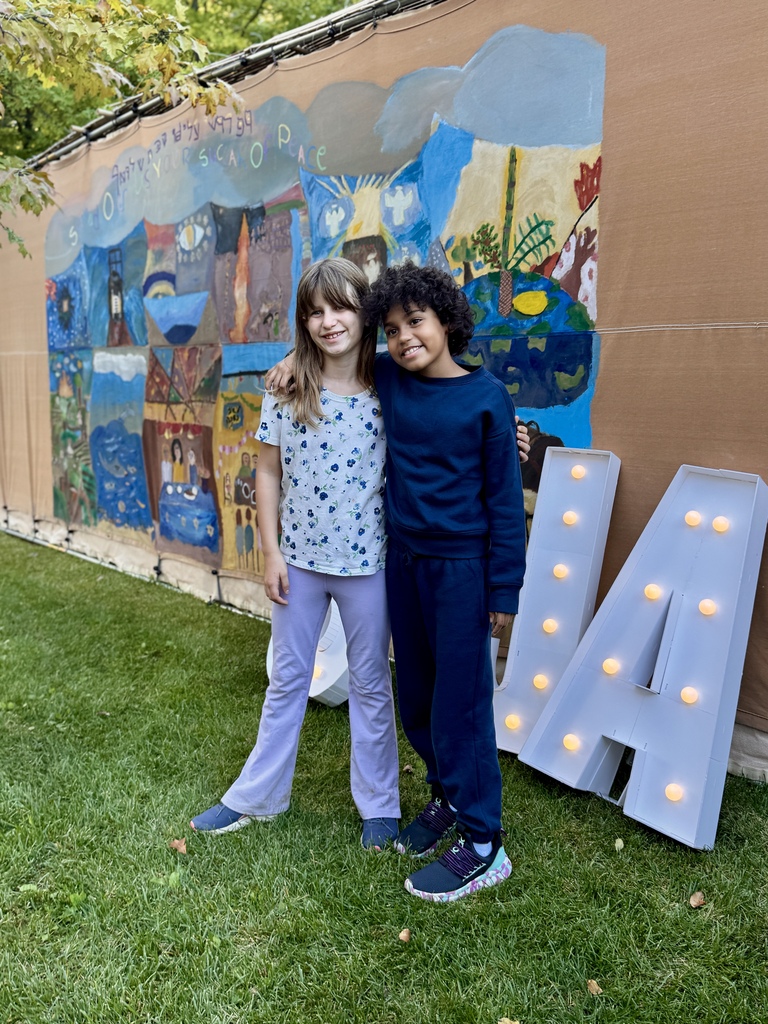 two students pose with S J A marquee letters in front of sukkah