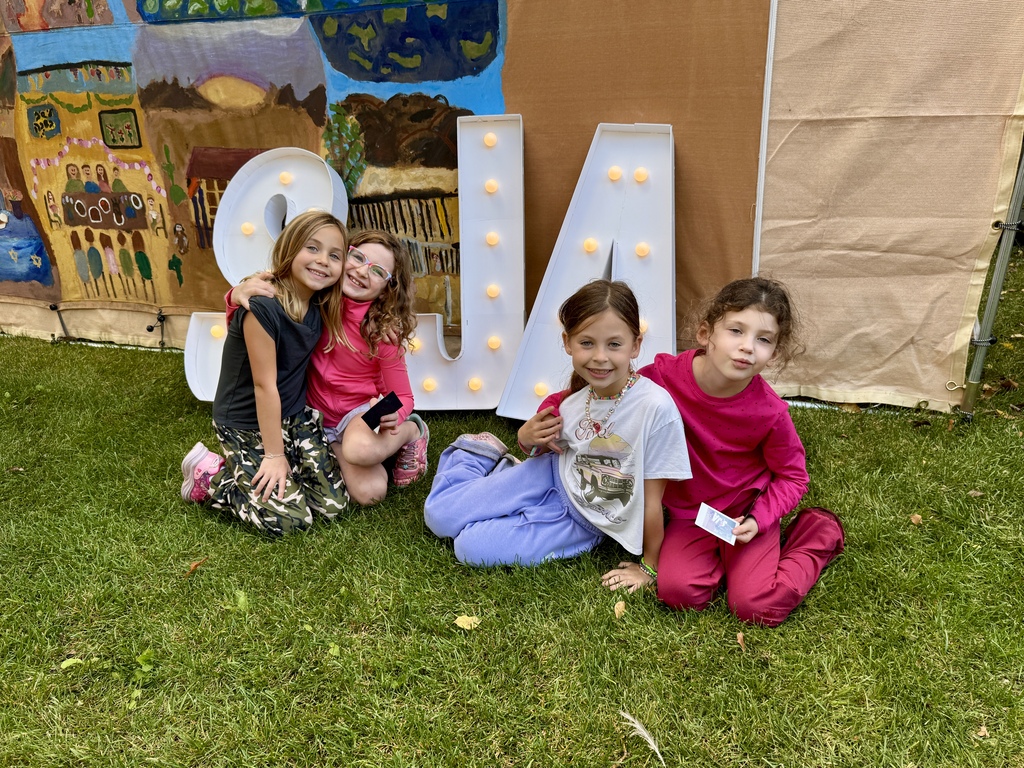 students pose with S J A marquee letters in front of sukkah