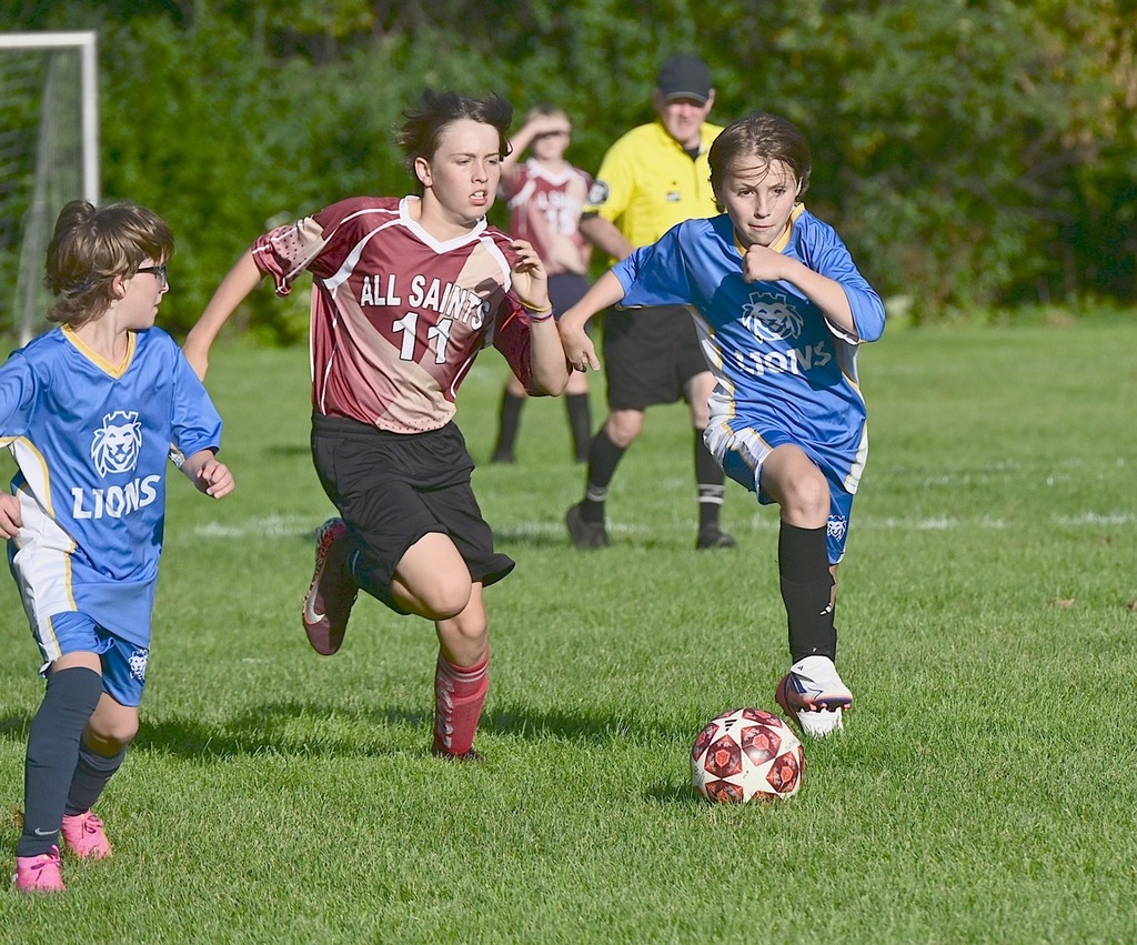 SJA Lions soccer player and opposing team member run behind ball