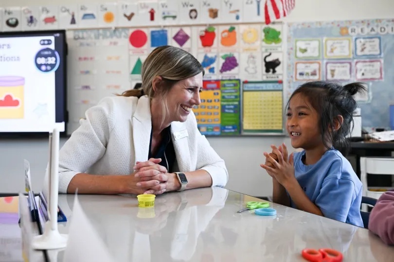 principal sitting and smiling with student at table in classroom