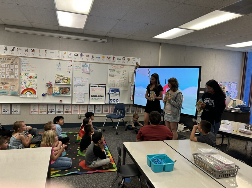 Hamiltion high kids reading to kinder students sitting on their reading rug.