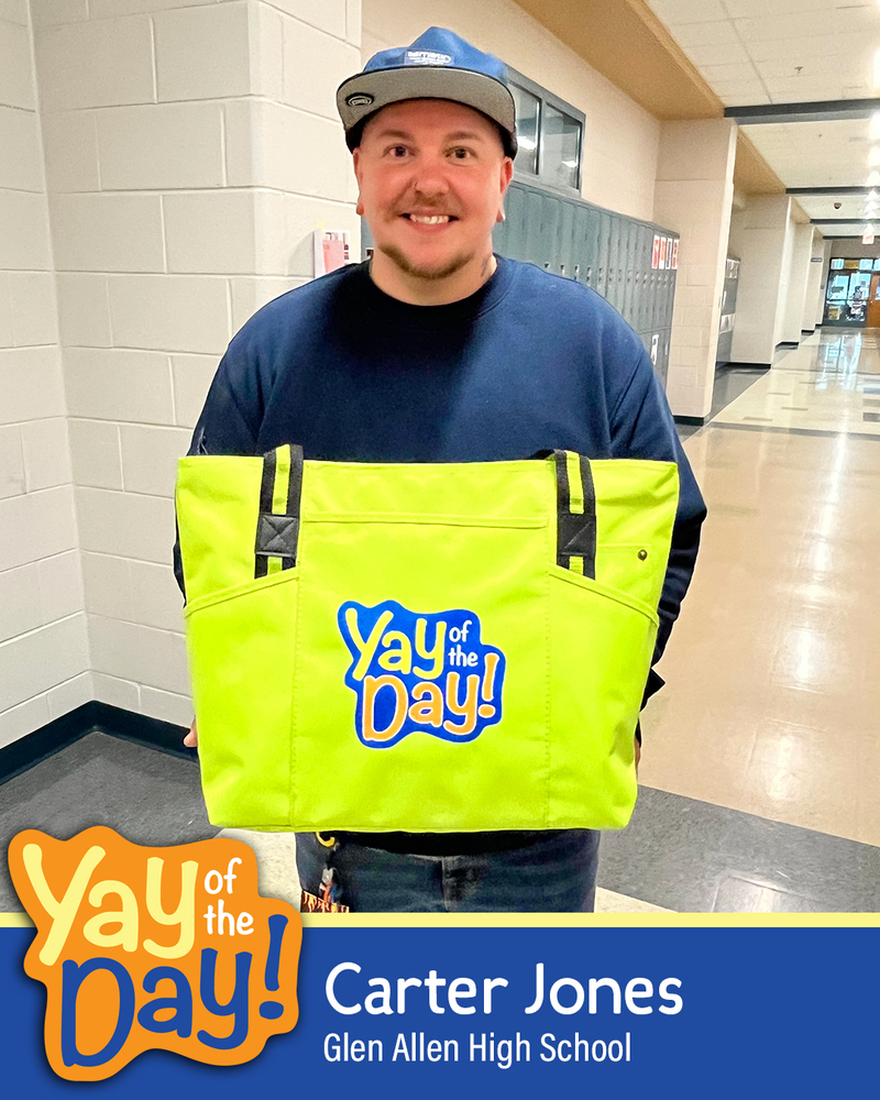Carter Jones of Glen Allen High School holds up a green Yay of the Day tote bag in a school hallway.