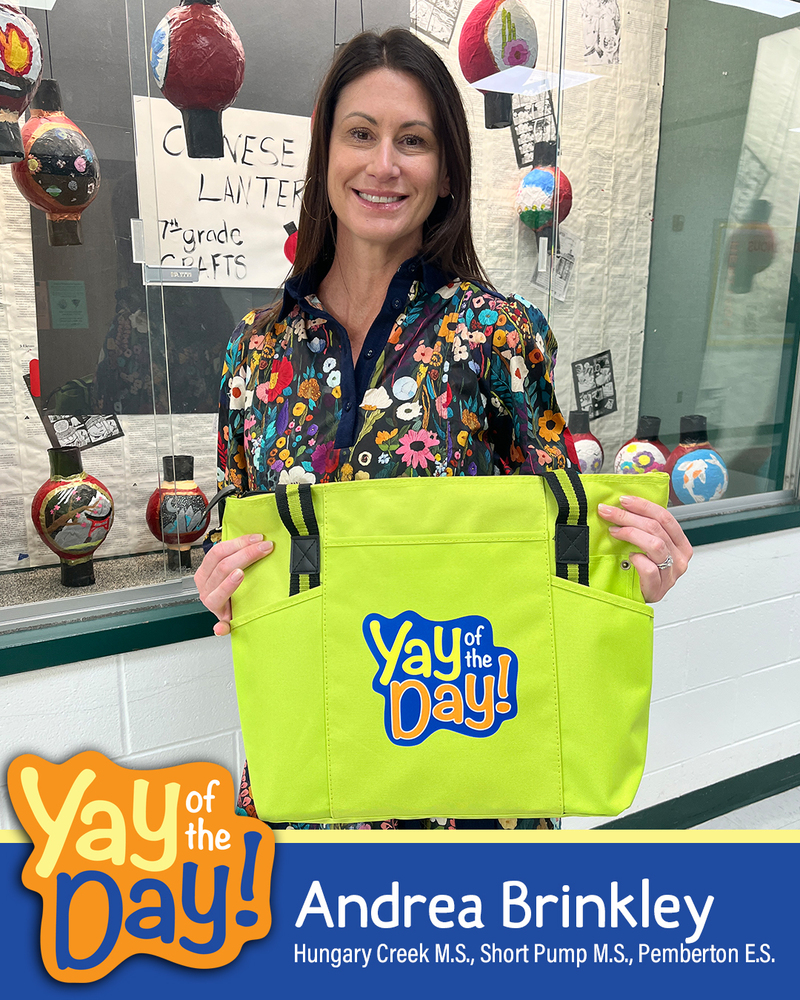 Andrea Brinkley holds up a Yay of the Day bag in front of a cultural display at a school. 