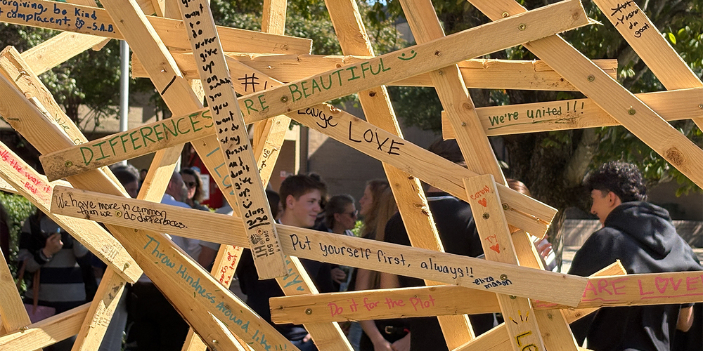 A sculpture made of wooden planks is adorned with positive messages written by students.