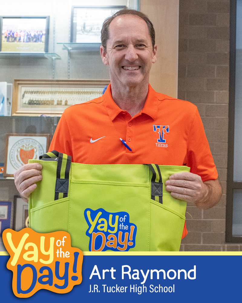 Principal Art Raymond of J.R. Tucker High School smiles and holds up a Yay of the Day tote bag.