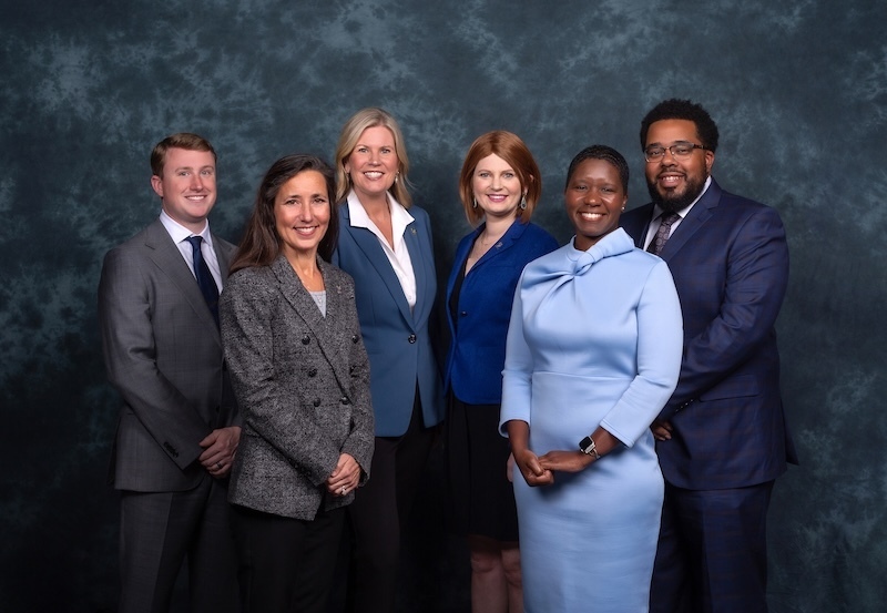 Members of the Henrico County School Board and leadership team posing together in formal business attire against a textured grey studio backdrop.