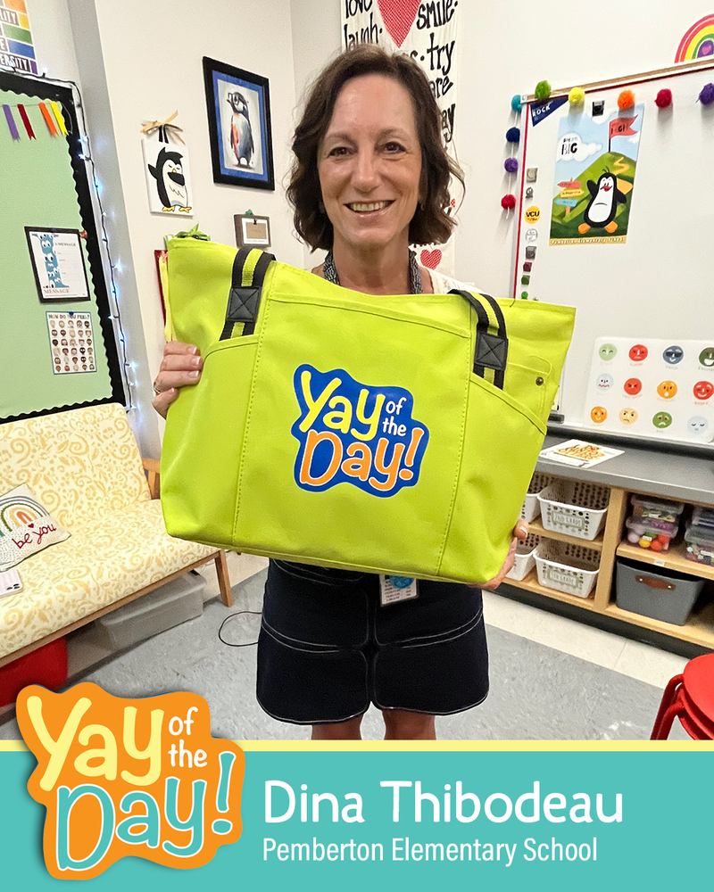A woman smiles and holds up a Yay of the Day bag in a classroom setting. The woman is identified with a graphic that reads Dina Thibodeau, Pemberton Elementary School.