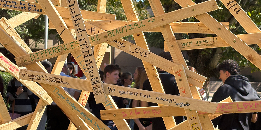 A sculpture made of wooden planks is adorned with positive messages written by students.