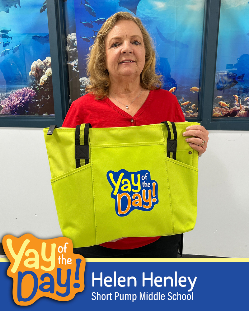 A woman smiles holding up a Yay of the Day bag in front of a school mural. The Yay of the Day recipient is identified as Helen Henley, Short Pump Middle School.