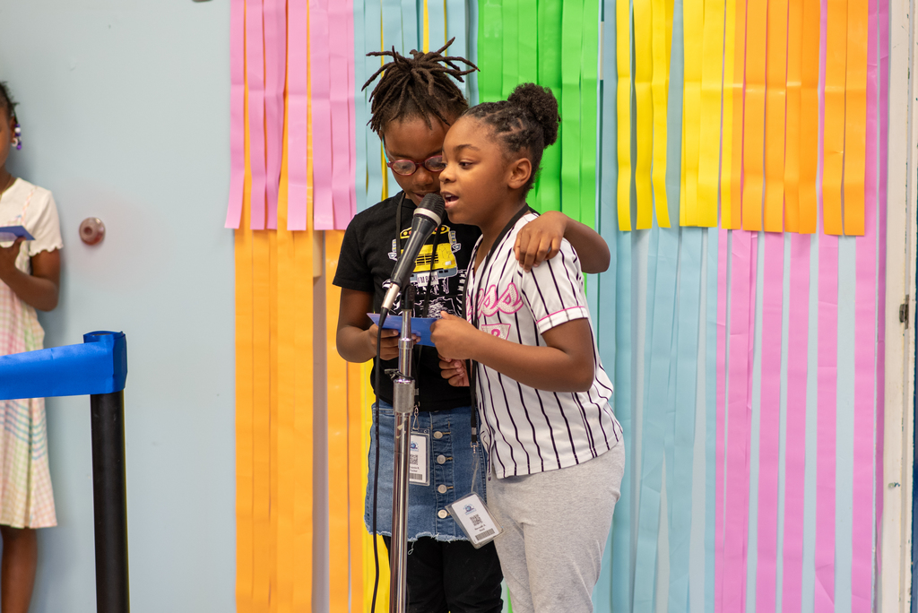 Two 3rd graders speak into a microphone