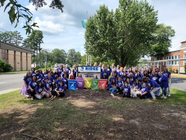 The photo shows Ridge Elementary staff smiling to welcome our students back by the elementary school sign!