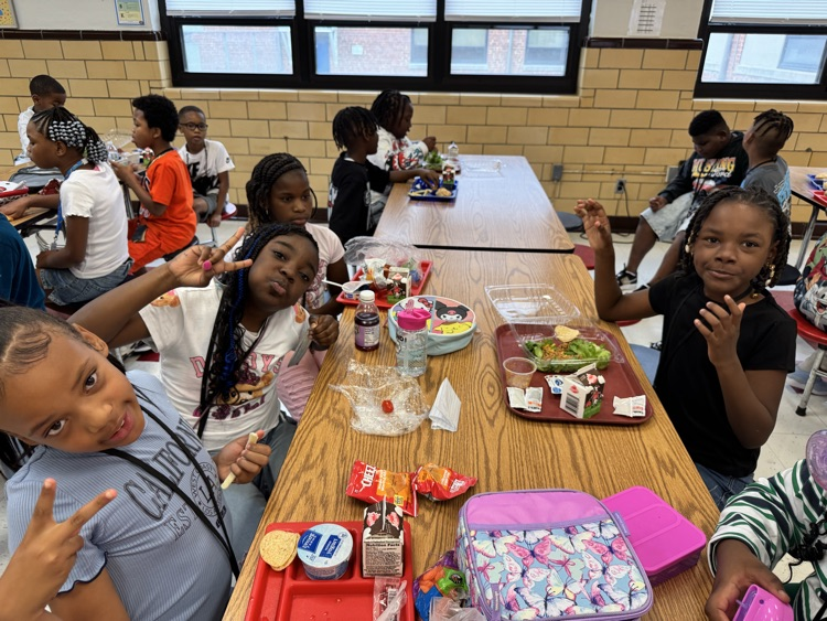 students make peace signs and smile at a cafeteria table 