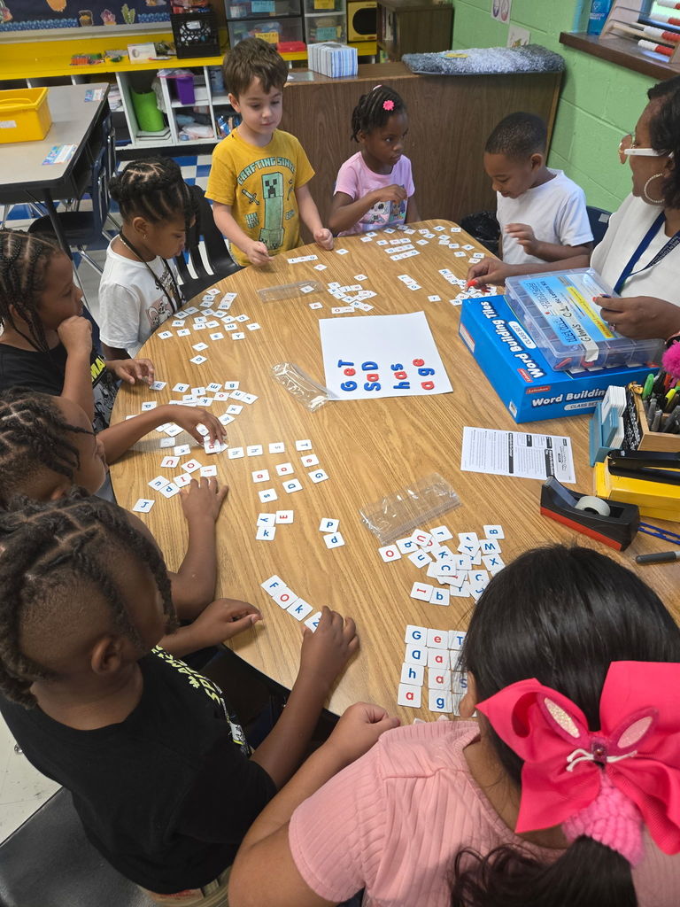 Students sit around a kidney table with their teacher to make words.