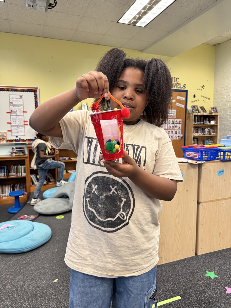 A student holds up a red cup that they used to design a way to feed animals.