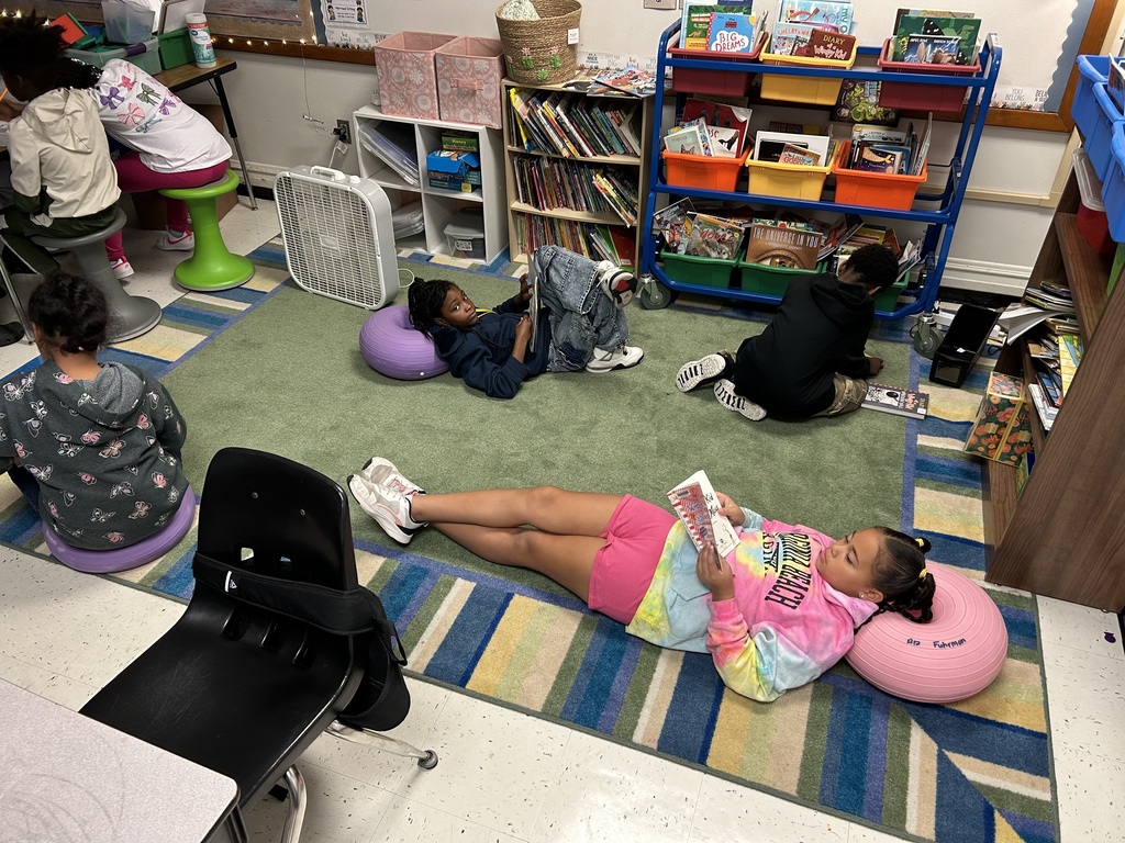Students lay on a rug and read their books.