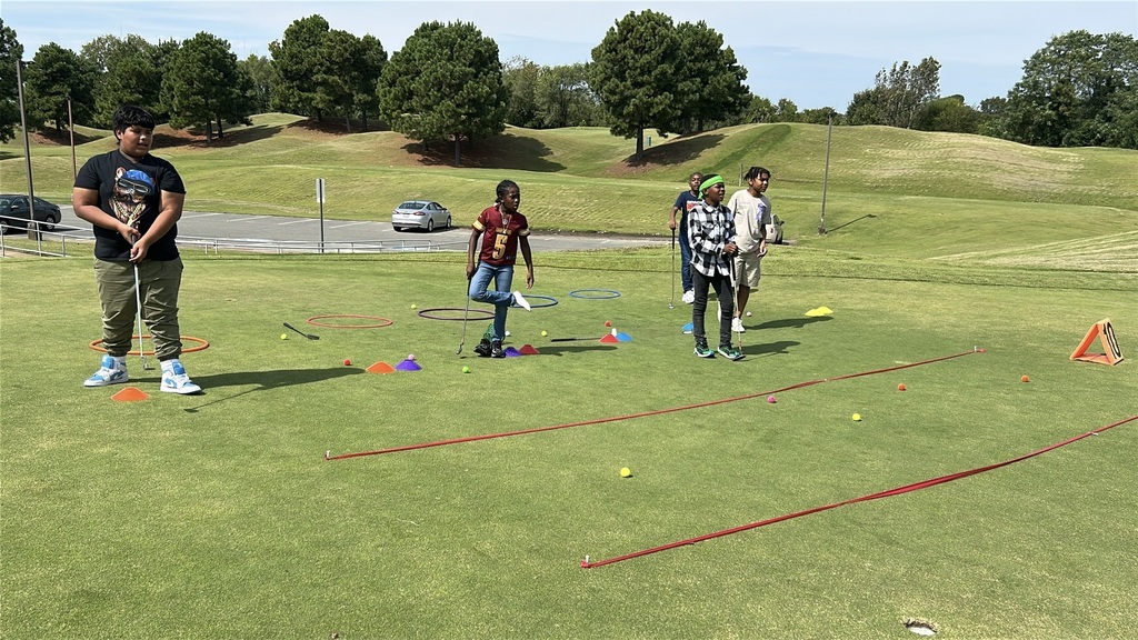 5th graders observe others while holding their golf clubs.