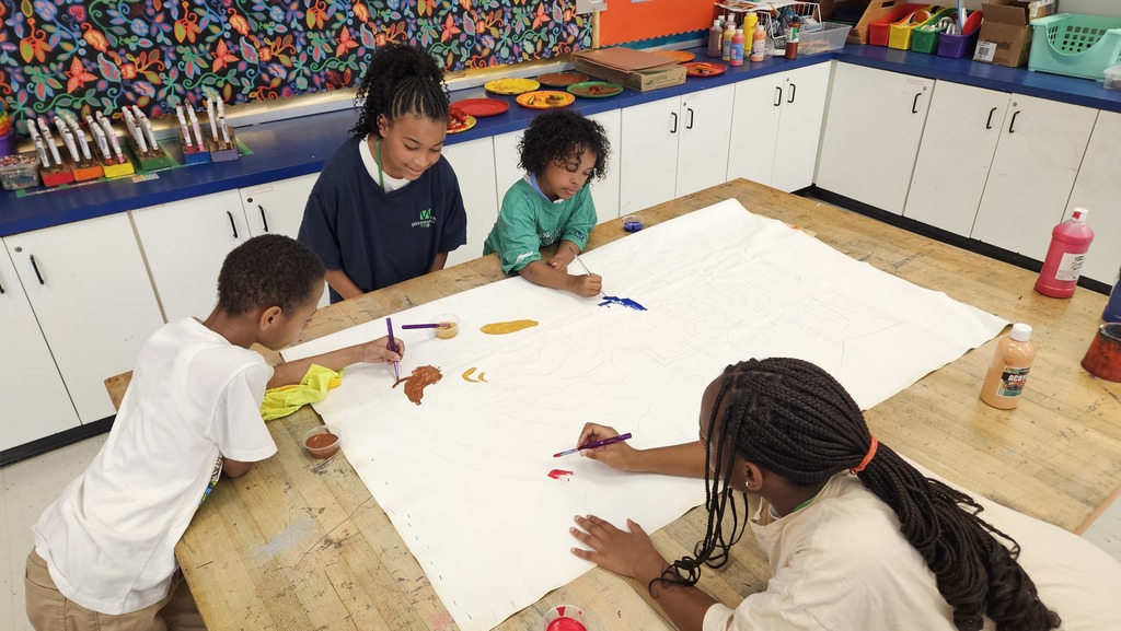Students paint a white canvas together.