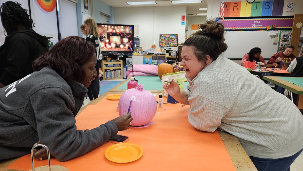 Staff smiling while they paint pumpkins.