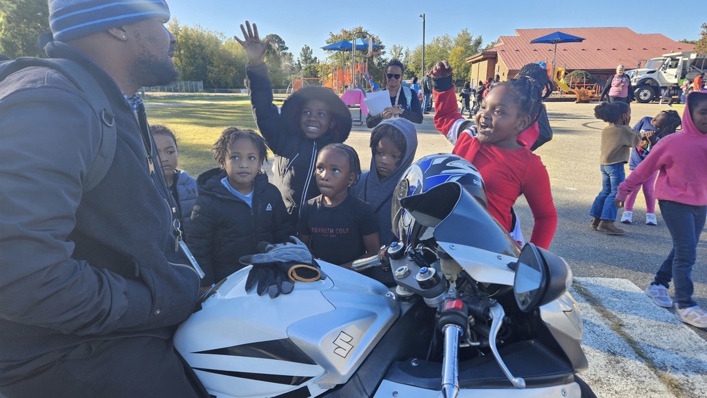 Students raise their hands and ask questions around a motorcycle.