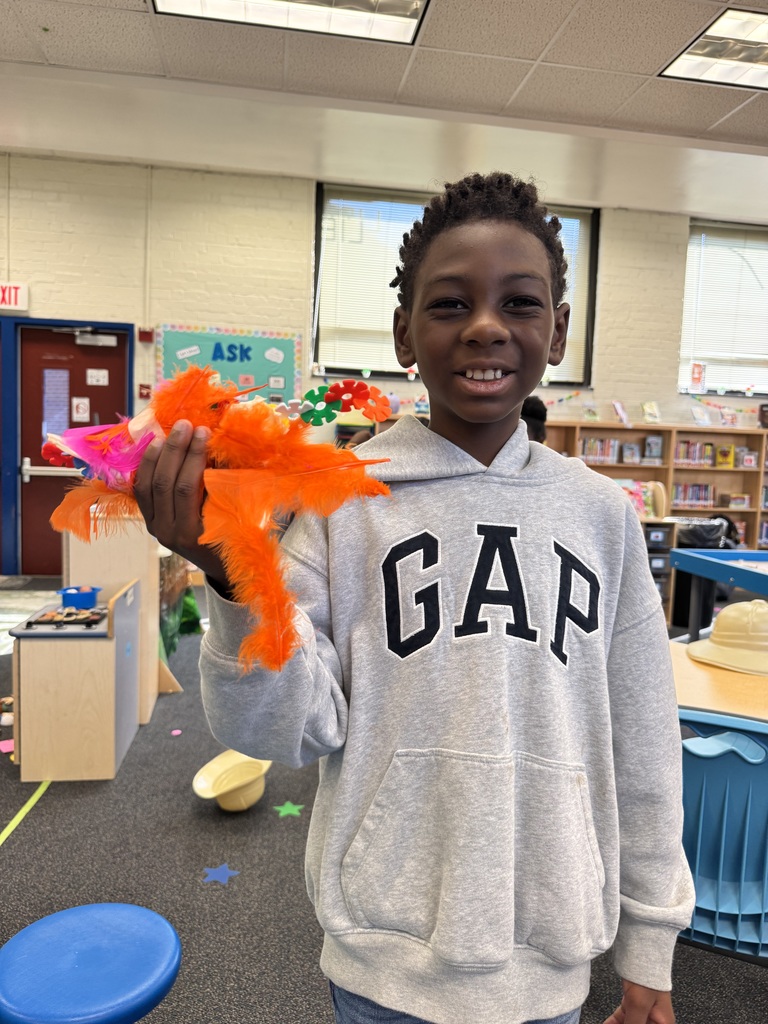 A student shows a dinosaur that he created using BrainFlakes and feathers.
