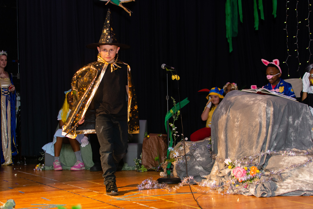 A student dressed in a wizard cape stands on stage.