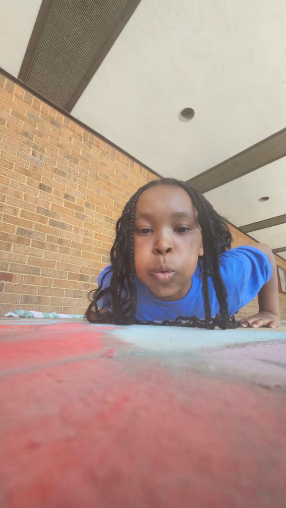 Student blows chalk dust off the sidewalk.
