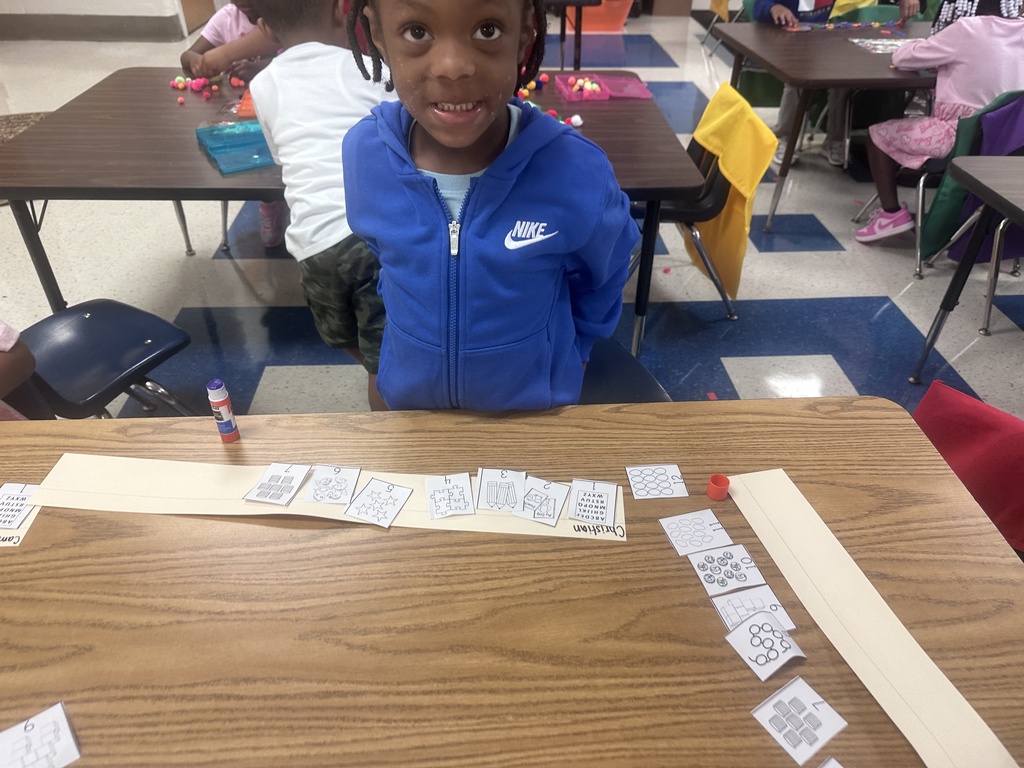 Student standing next to their desk showing off thier paper and glue project.
