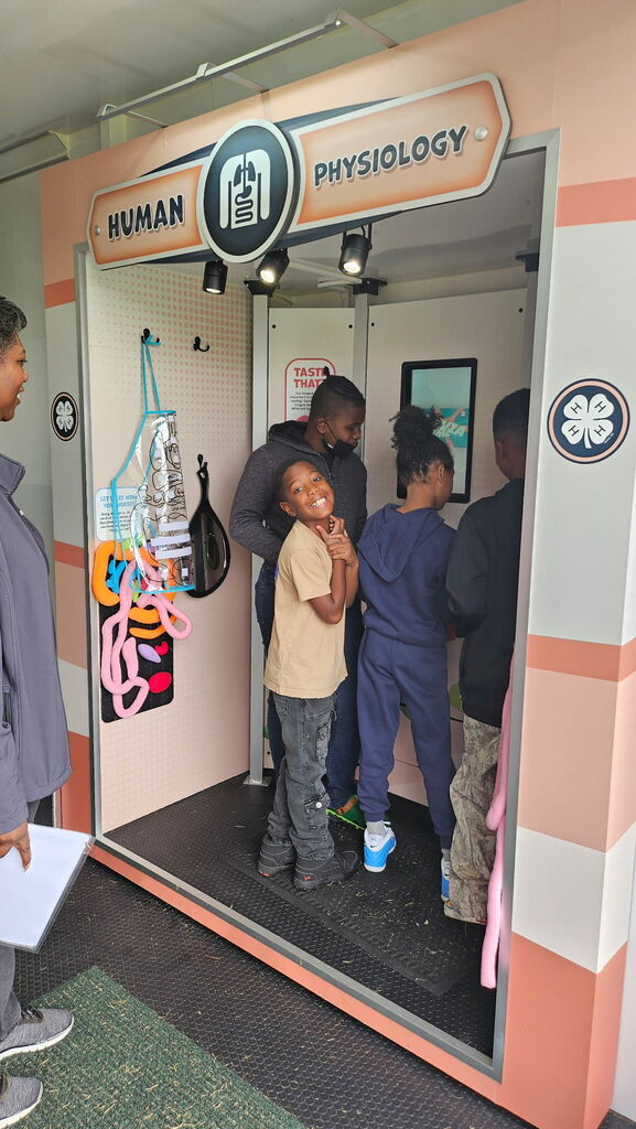 Four students stand at a science exhibit on Human Physiology, while one turns toward the camera smiling.