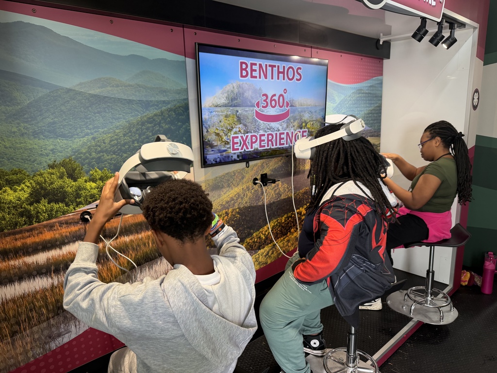 Three students sit infront of a screen with VR headsets on.