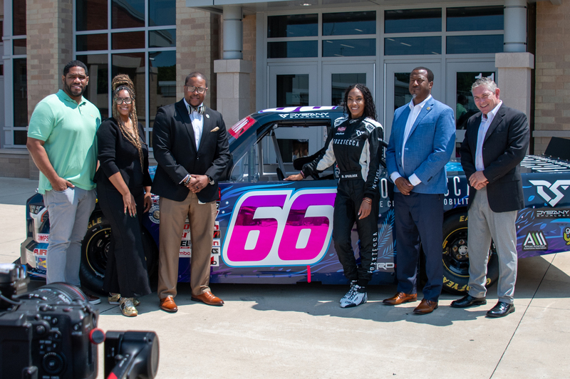 A group of people pose with a race truck in front of Highland Springs High School.