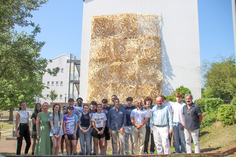 A group of students and adults pose for a photo in front of a wooden sculpture in Germany.
