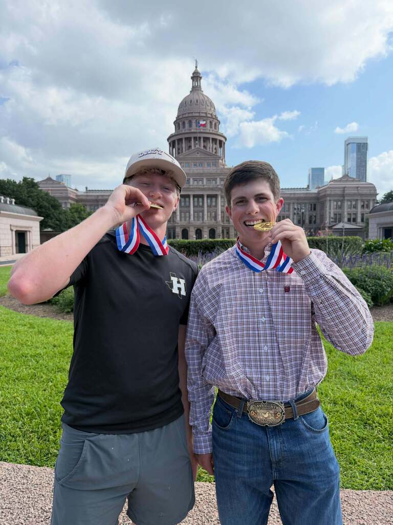 Two men standing in front of a large building with gold medals around their necks.