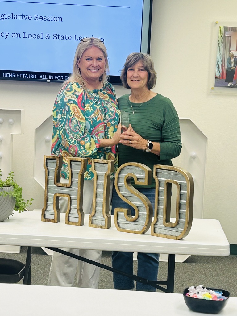 Two women standing behind a table with large letters spelling HISD. A bowl of candy is on the table.
