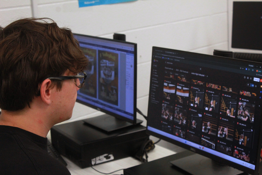 Person wearing glasses at a desk with two computer monitors; one displays a design, the other a grid of images.