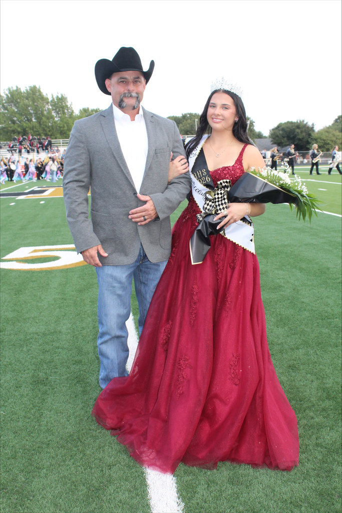 A man and a woman stand on a football field, she holds a bouquet of flowers.