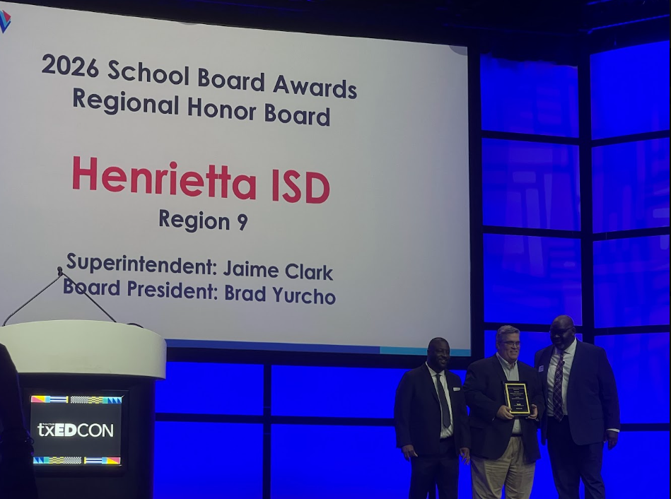 Four men stand at a podium, one holding an award, in front of a screen. Text reads "2026 School Board Awards."