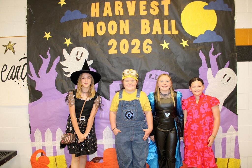 Four girls in costumes stand in front of a banner that reads Harvest Moon Ball 2026.