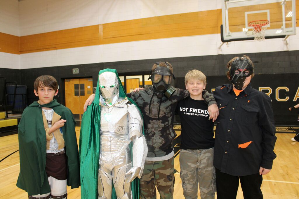 Five students stand together on a basketball court. Four wear costumes; one is silver, one is green, one has a gas mask, and one has a black mask.