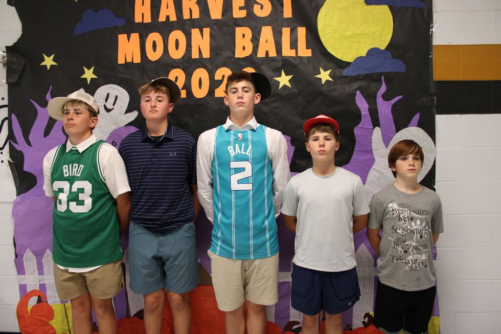 Five boys stand together in front of a decorated backdrop with the words Harvest Moon Ball.