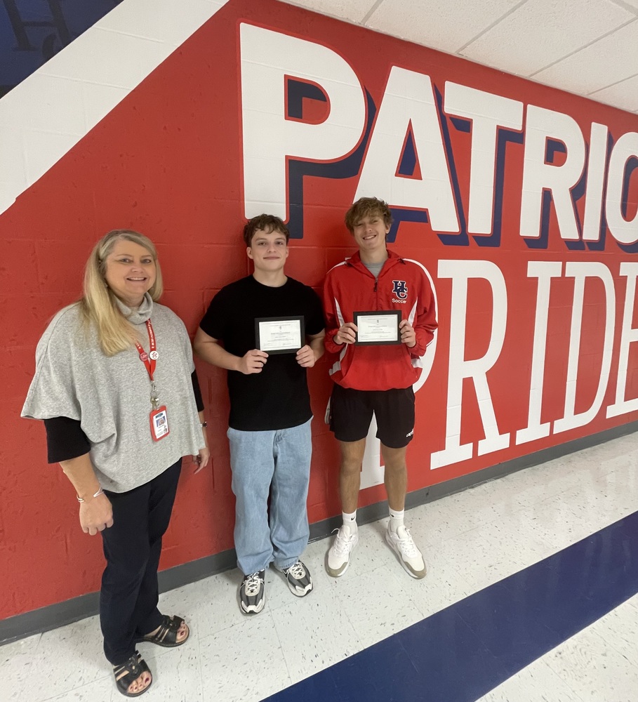 two male students standing with principal in front of Patriot Pride mural