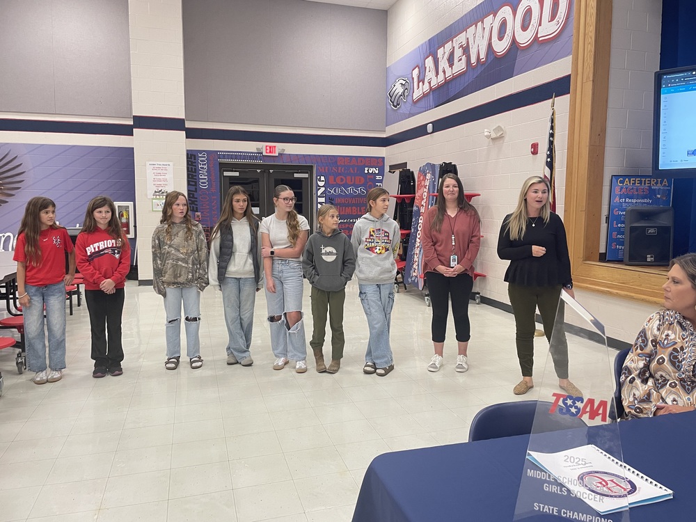 middle school girls and coaches present trophy to board