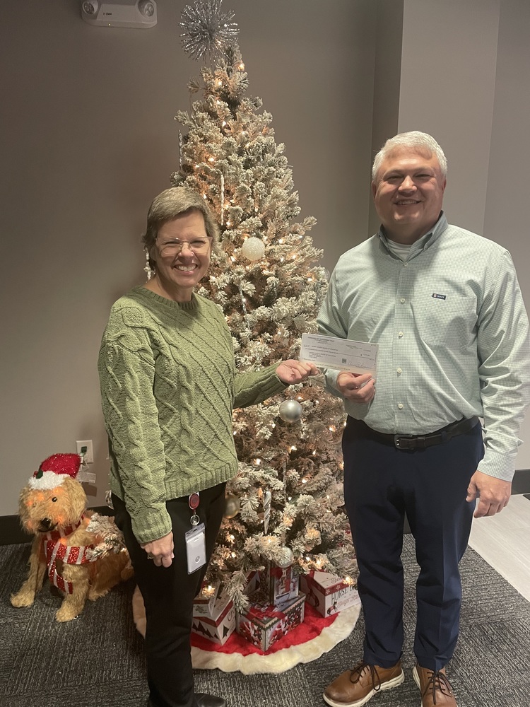 two people holding a check in front of Christams tree