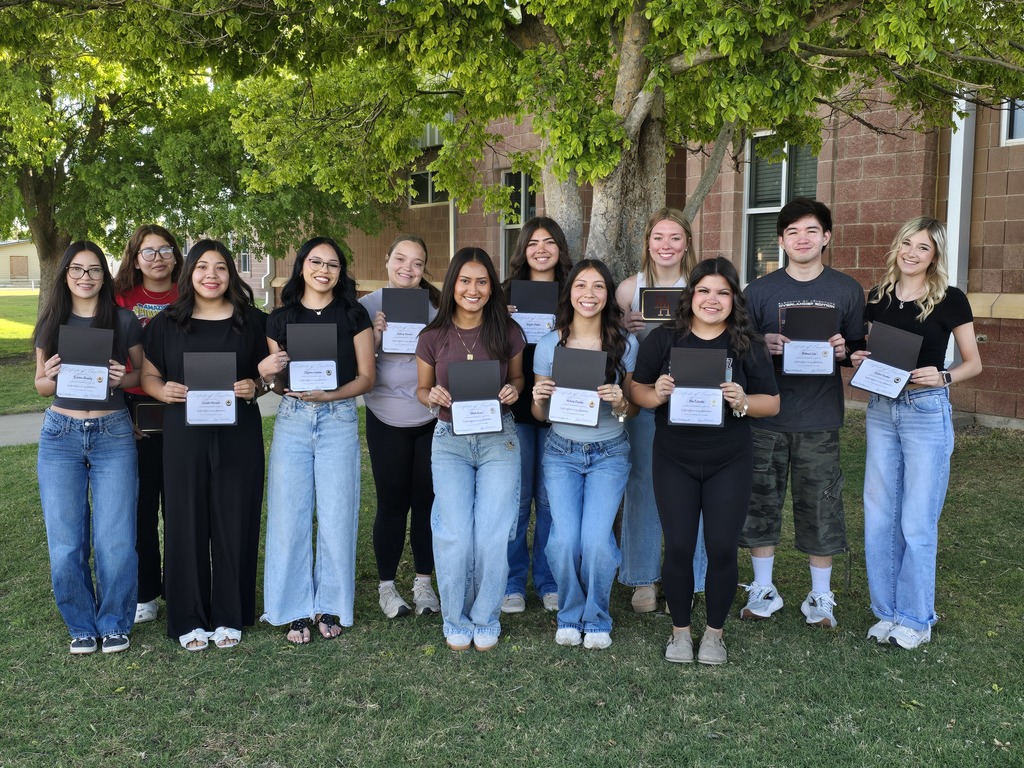 Group of young people holding certificates, posing for a photo outside a building with trees.