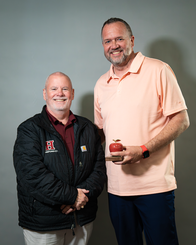 Two men standing against a light gray background, one holding a red apple, both wearing smiles.