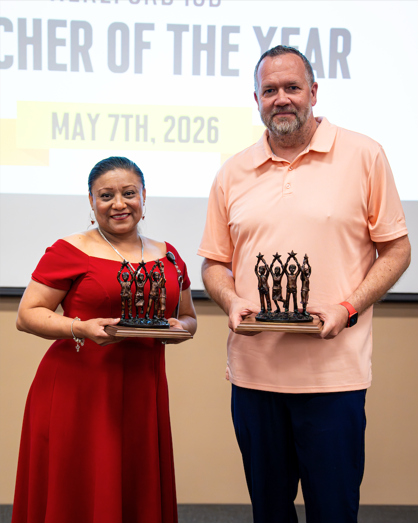 Two people holding awards in front of a screen that reads "Teacher of the Year, May 7th, 2026".